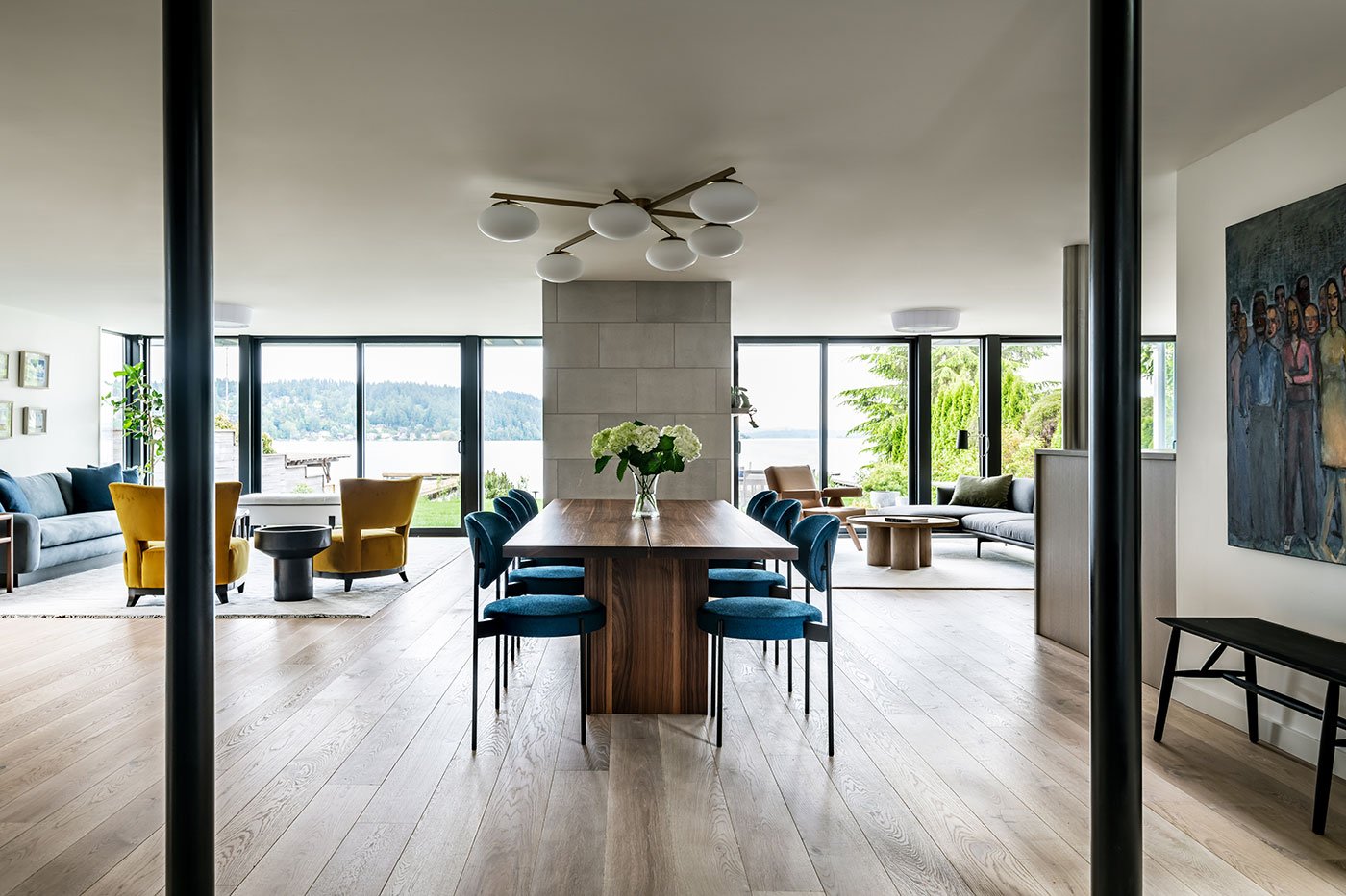 An open concept space with dining table and two living spaces facing a lakefront.