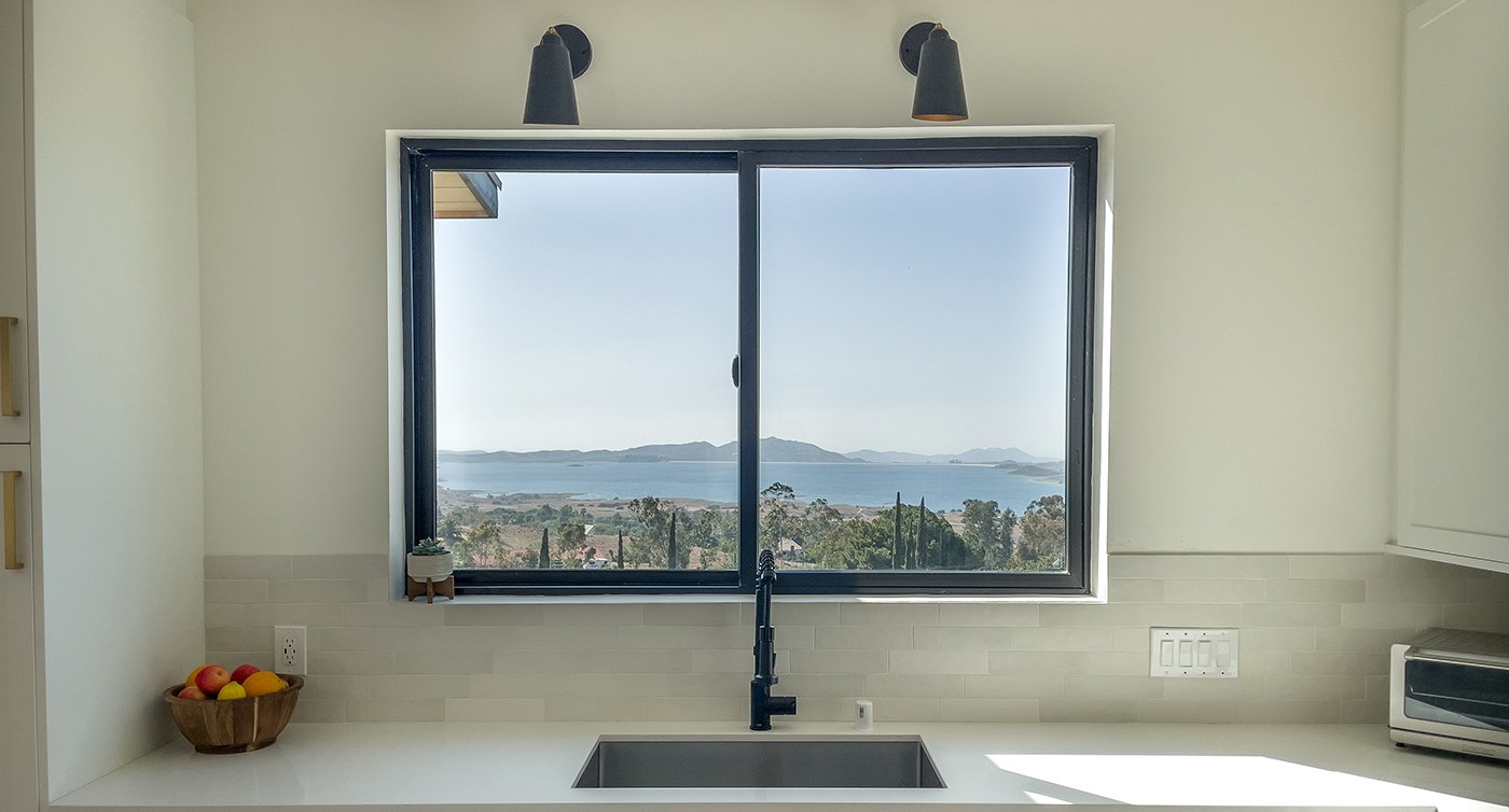 A kitchen with a view of a mountainous coastline thanks to the Andersen® 100 Series Gliding Window above the sink.