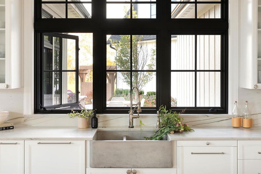 A European farmhouse kitchen featuring black casement windows over a rustic concrete apron sink