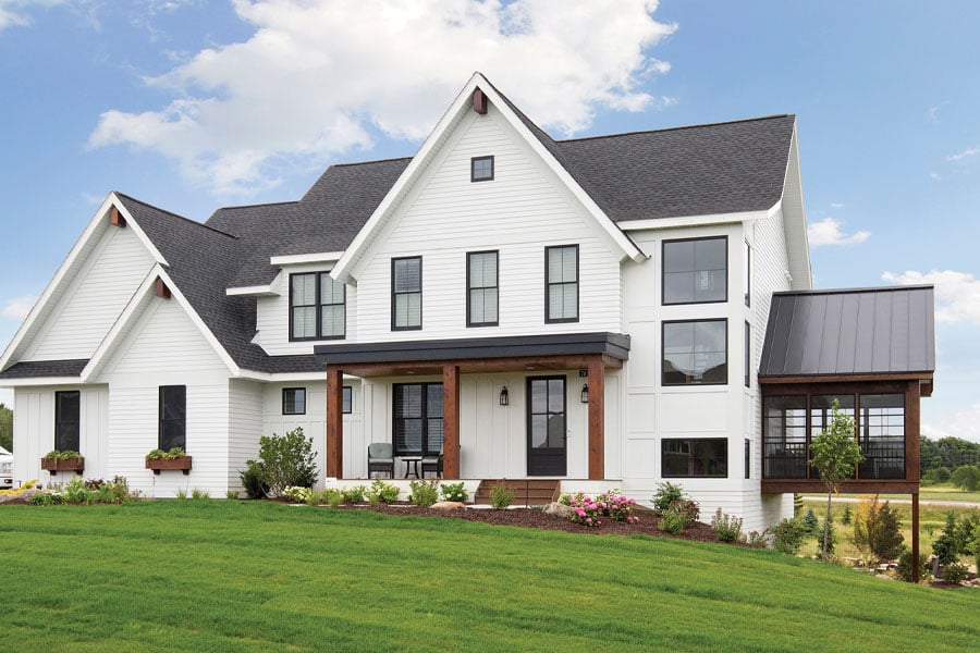 white farmhouse styled home with black framed Andersen windows in daytime with green grass and blue sky