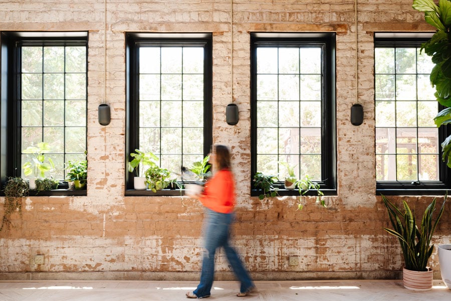 A row of four black windows with colonial grilles in a historic home with exposed brick walls.