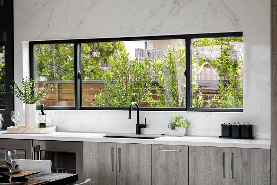 A kitchen with a marble backsplash and an extra wide Andersen® 100 Series Gliding Window with three sashes.