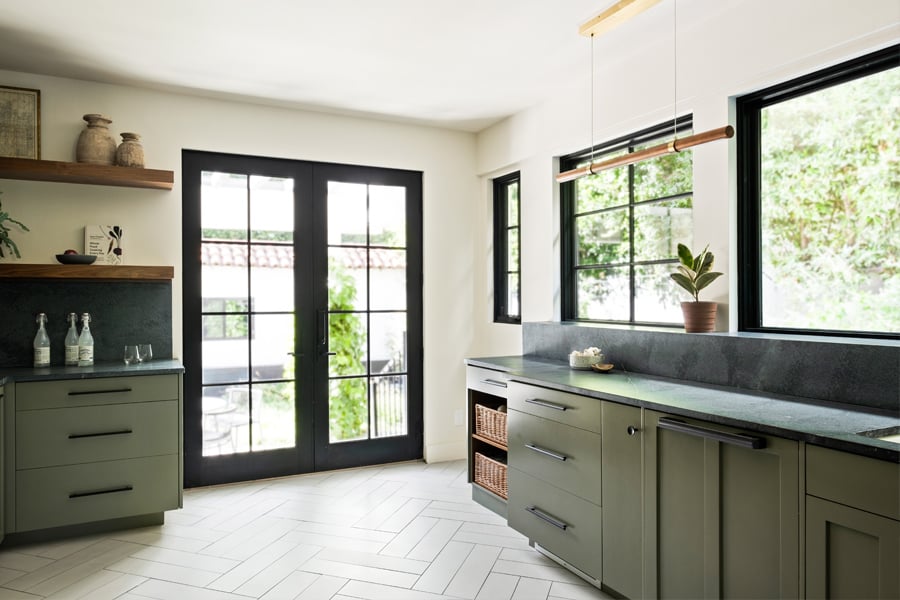 A kitchen with green cabinetry, black soapstone countertops and lots of windows and doors, including a black-framed set of Andersen E-Series Hinged Patio Doors.