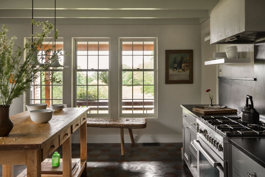 A pastoral kitchen with three large double-hung windows featuring cottage sashes that face a garden.