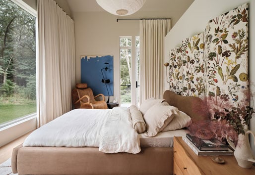 A bedroom with a large picture window at the end of the bed and a hinged door with sidelights and transoms leading out to a deck.