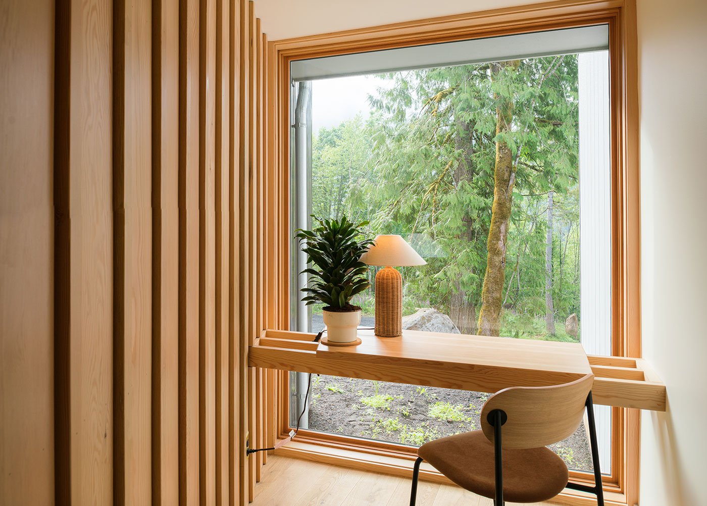 A desk that floats in front of a monumental picture window that begins at the floor and affords views of the forest outside.
