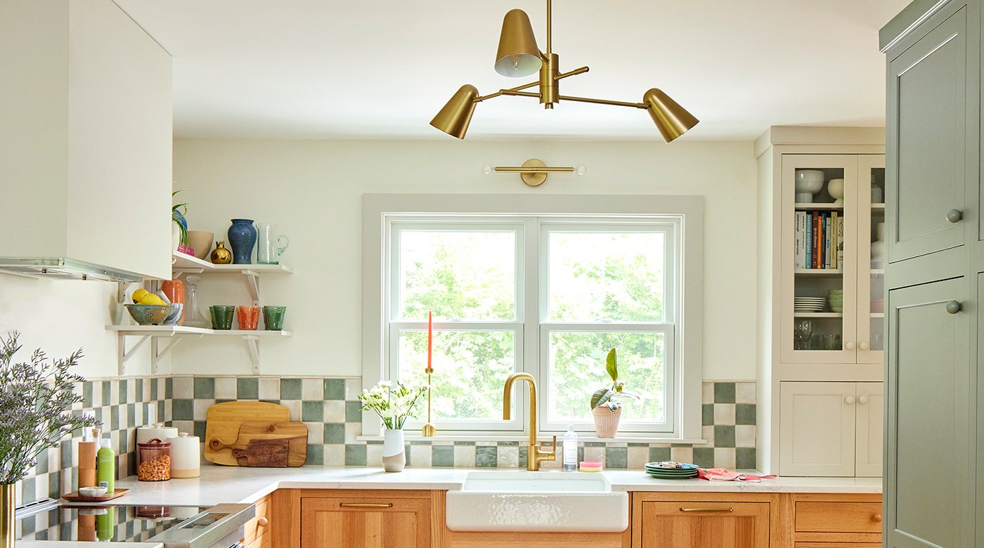 A kitchen with checkerboard backsplash, warm wood cabinetry and floors, and Andersen® 200 Series Double-Hung Windows above the kitchen sink.
