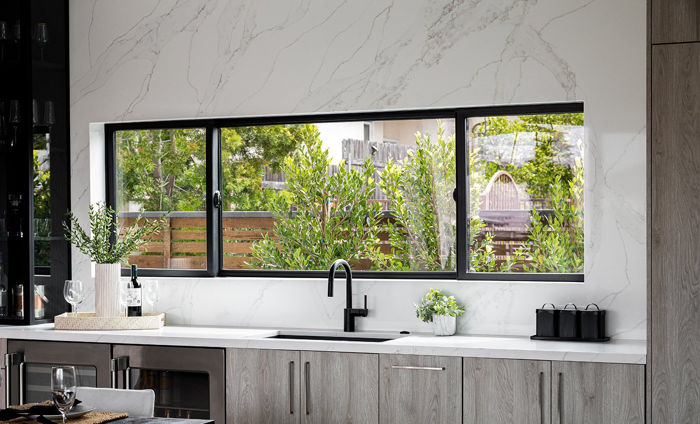 A kitchen with an extra-wide Andersen® 100 Series Gliding Window installed into a marble backsplash above the sink.