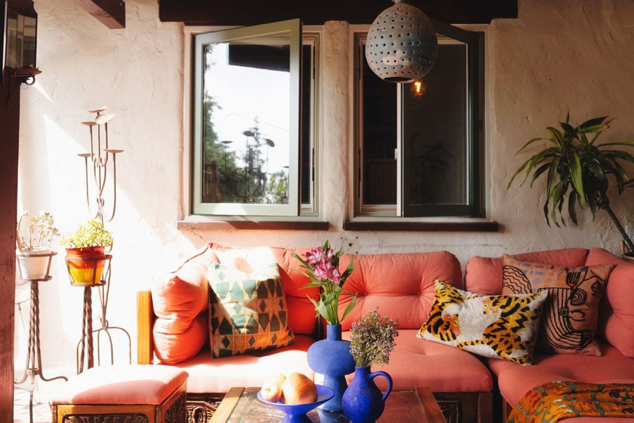 Justina Blakeney stands in front of the E-Series Gliding Patio Door on her lanai, on the left, and an exterior shot showing an outdoor seating area with couch, coffee table, footstool, and potted plants, on the right.