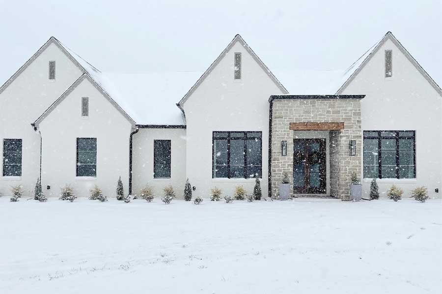 A white house with black Andersen windows and a stone entryway makes for a striking look, even in a snowstorm.