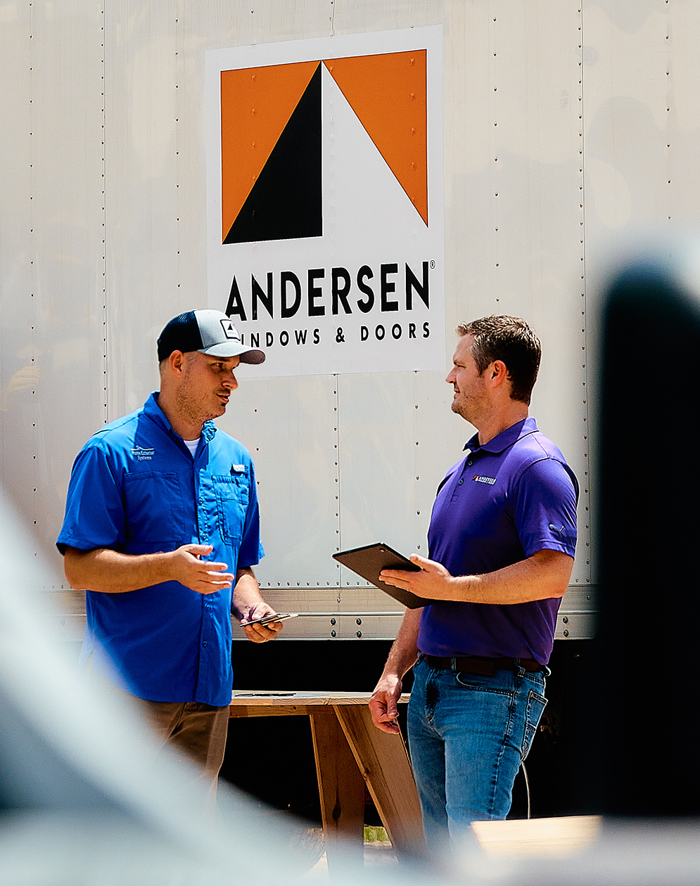 Two men chatting in front of an Andersen Windows truck