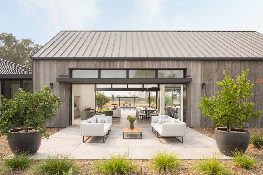 An exterior shot of a black Andersen® MultiGlide™ Door that opens an entire wall to provide a seamless indoor/outdoor space between living room and courtyard.