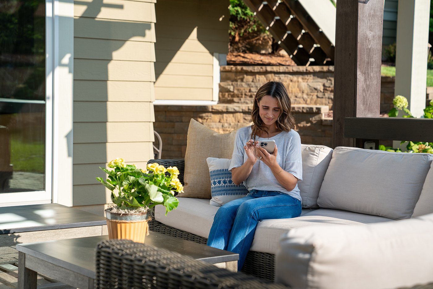 A woman seated on an outdoor couch reads her phone.