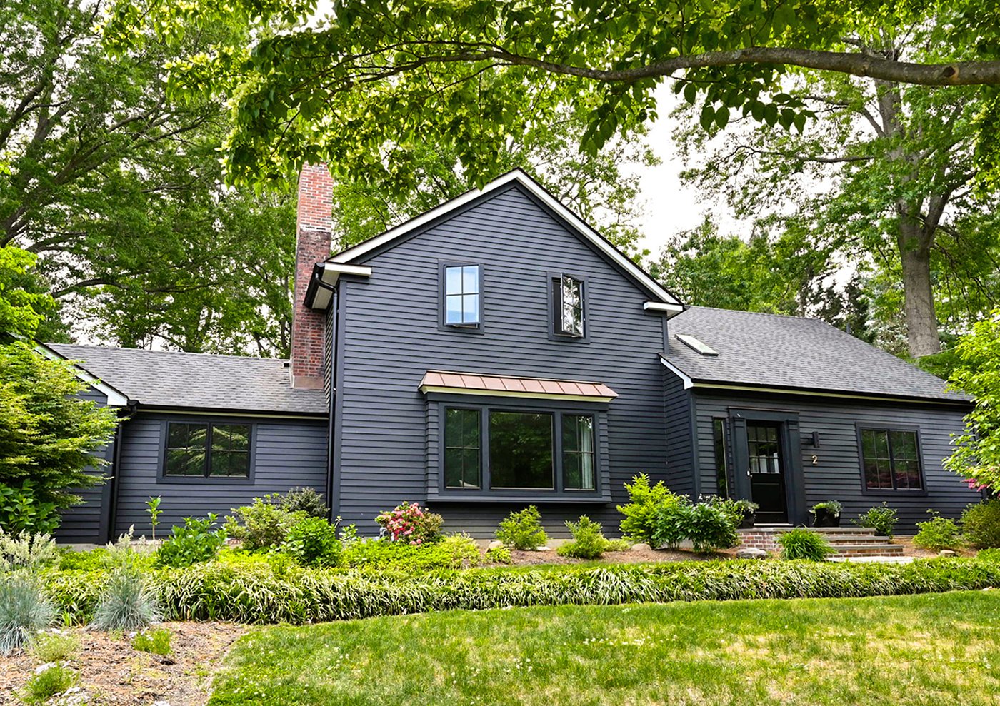 An exterior shot of a black Cape Cod home with black windows, including a prominent living room window combination.