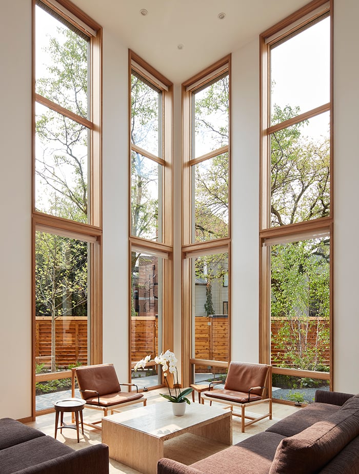 double-height living room with floor-to-ceiling windows that have natural wood frames.